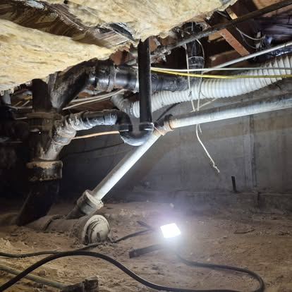 Crawlspace pipes and worklight during an inspection